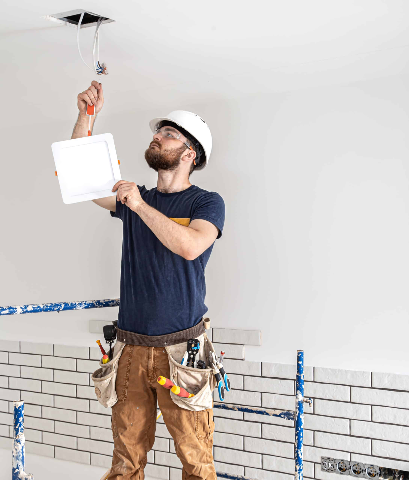 Électricien installant un luminaire encastré sur un chantier neuf